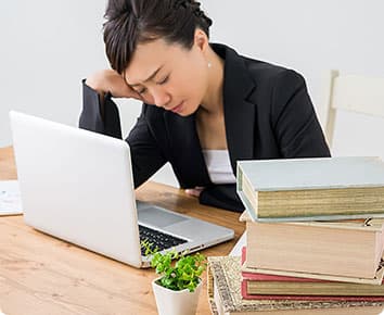 ノートパソコンを疲れた様子で見つめる女性